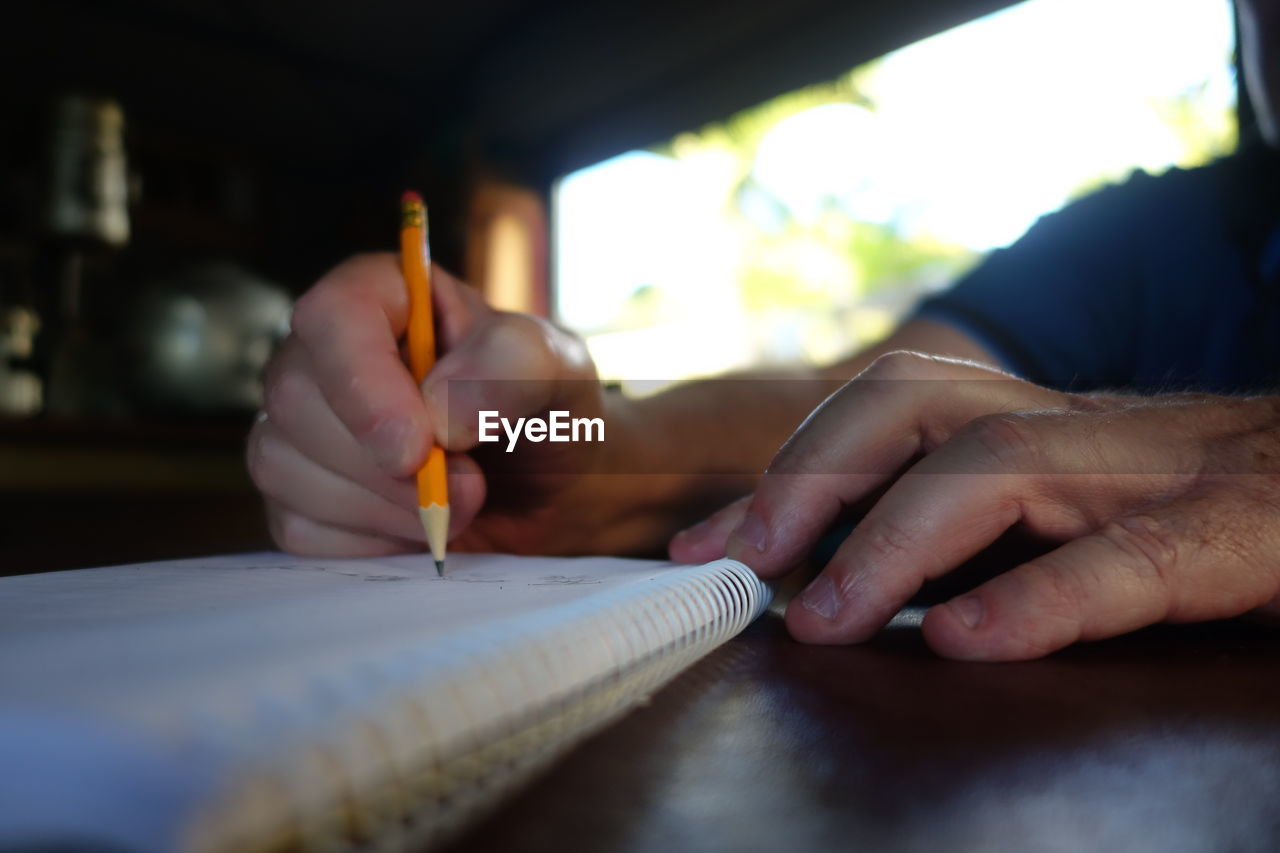 Cropped hands of man writing on book