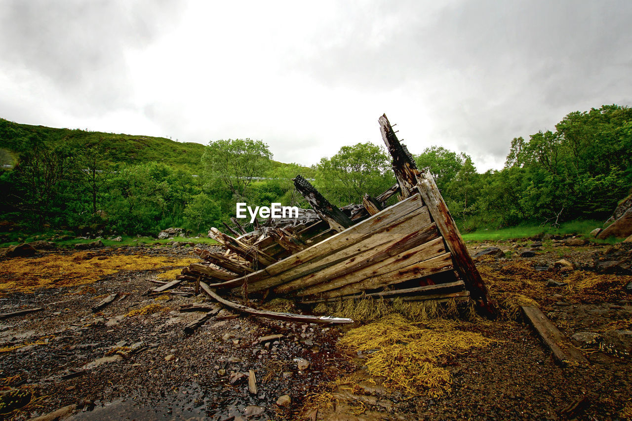 DAMAGED WOODEN STRUCTURE ON FIELD AGAINST SKY