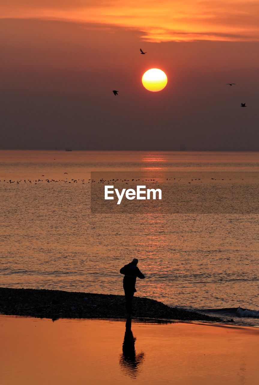 SILHOUETTE MAN STANDING ON BEACH DURING SUNSET