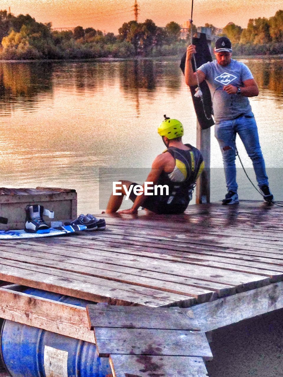 MEN SITTING ON WOODEN POST IN WATER