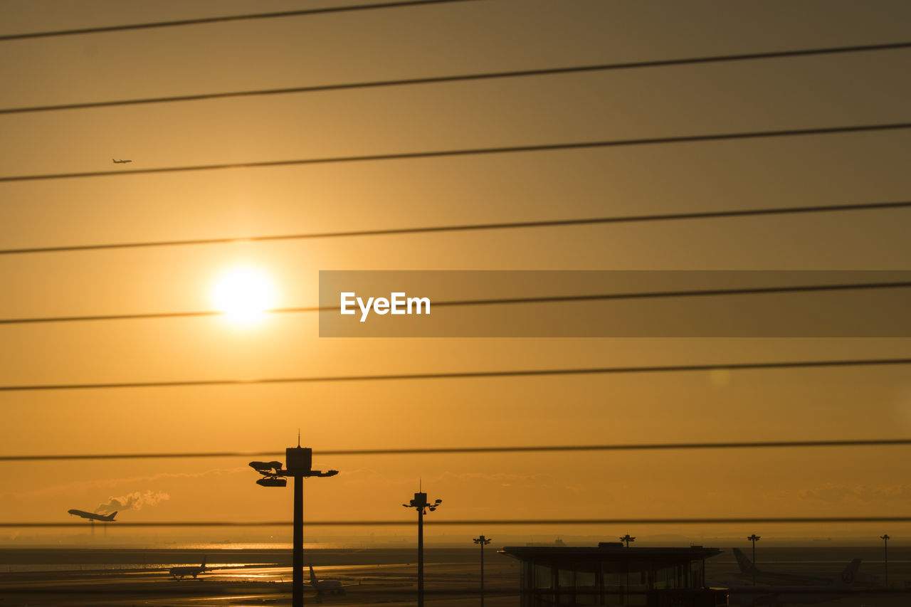 Low angle view of silhouette cables against orange sky