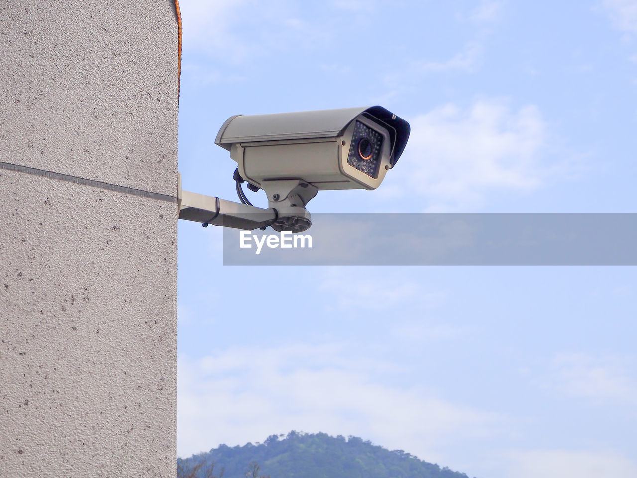 Low angle view of security camera on wall against blue sky