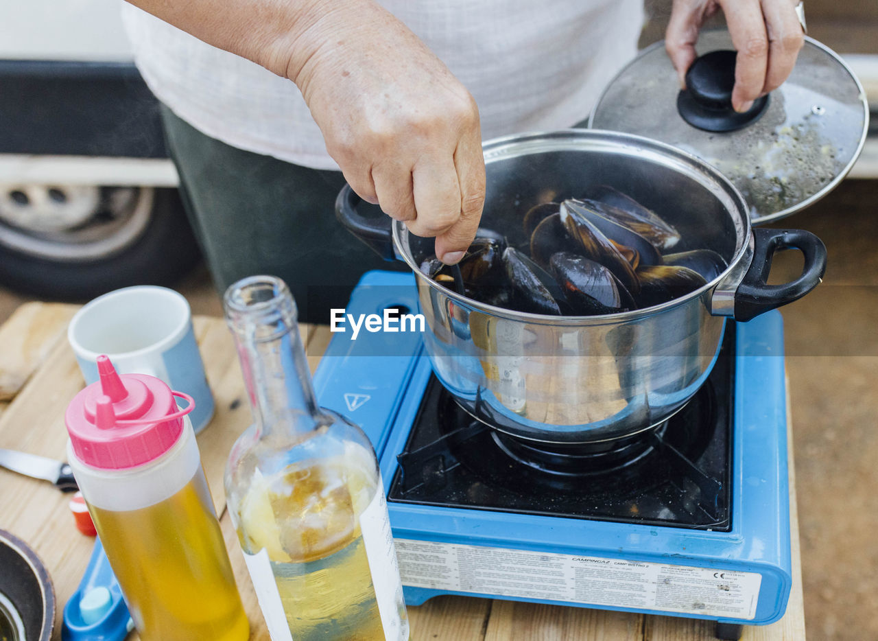 Senior woman cooking mussels in camping gas on in her van