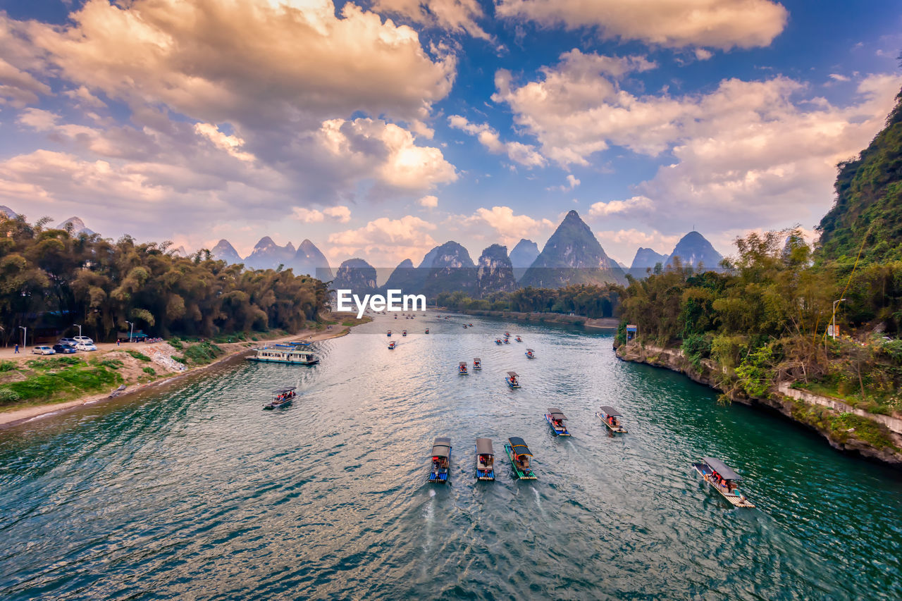 PEOPLE ON BOATS IN SEA AGAINST MOUNTAINS