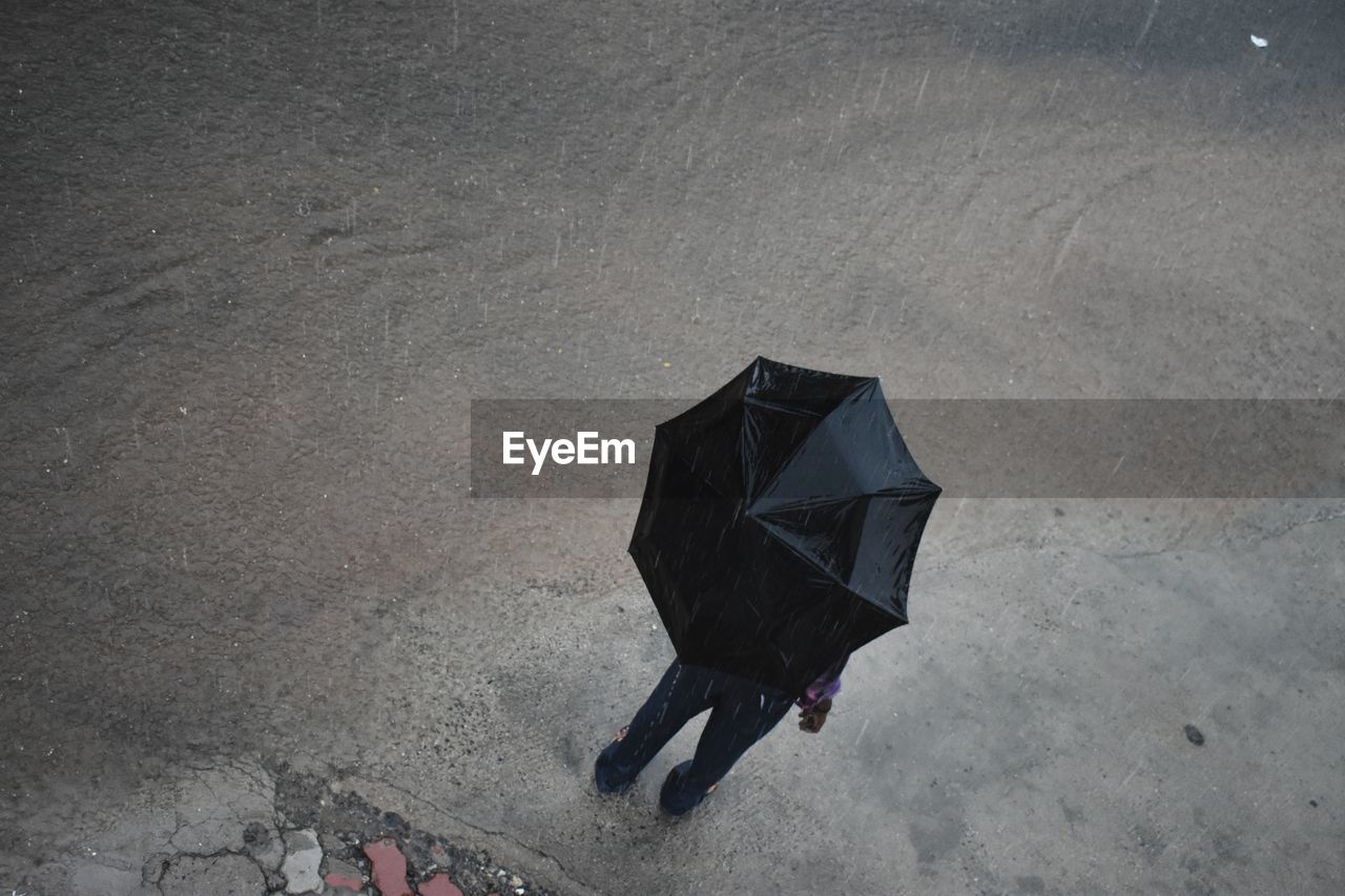 High angle view of man with umbrella standing on road during rainy season