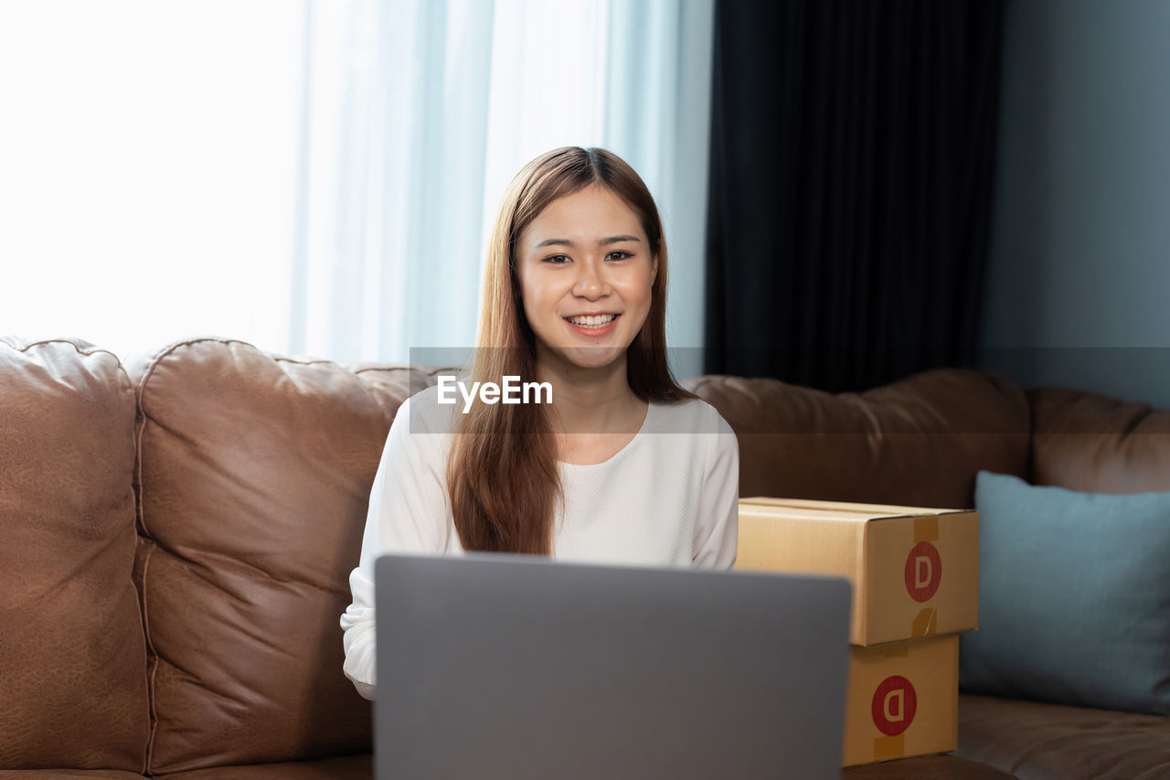 young woman using laptop while sitting on sofa at home