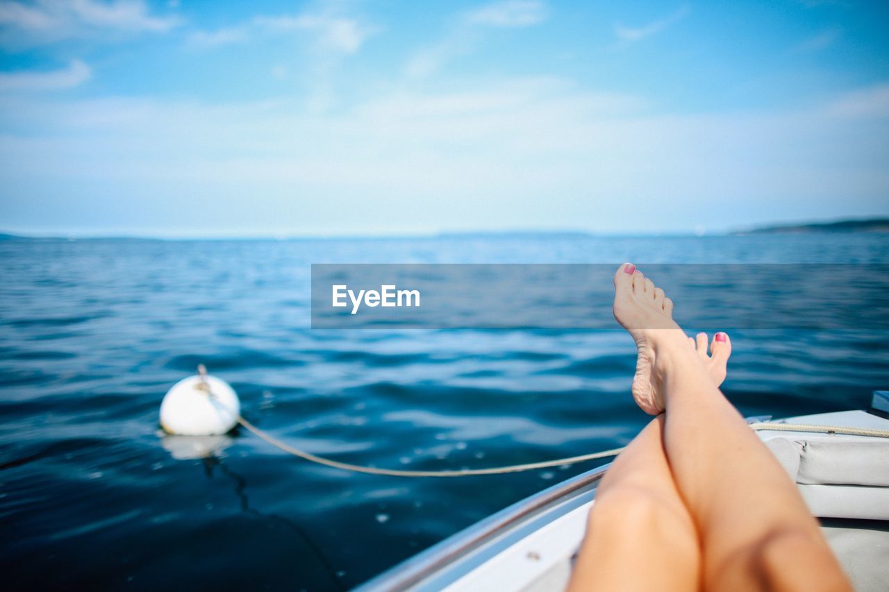 Low section of woman relaxing on boat in sea against sky