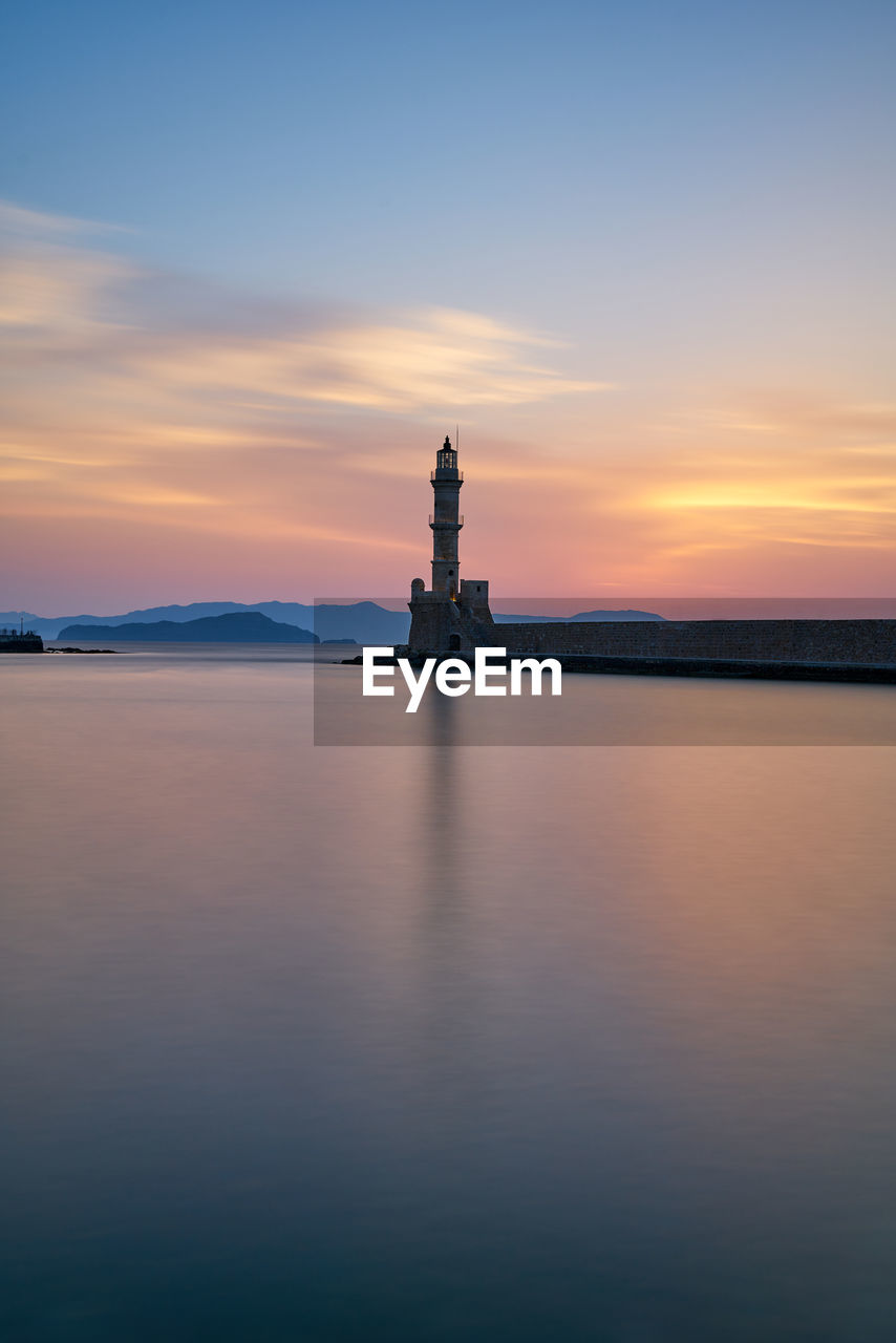 Lighthouse by sea against sky during sunset