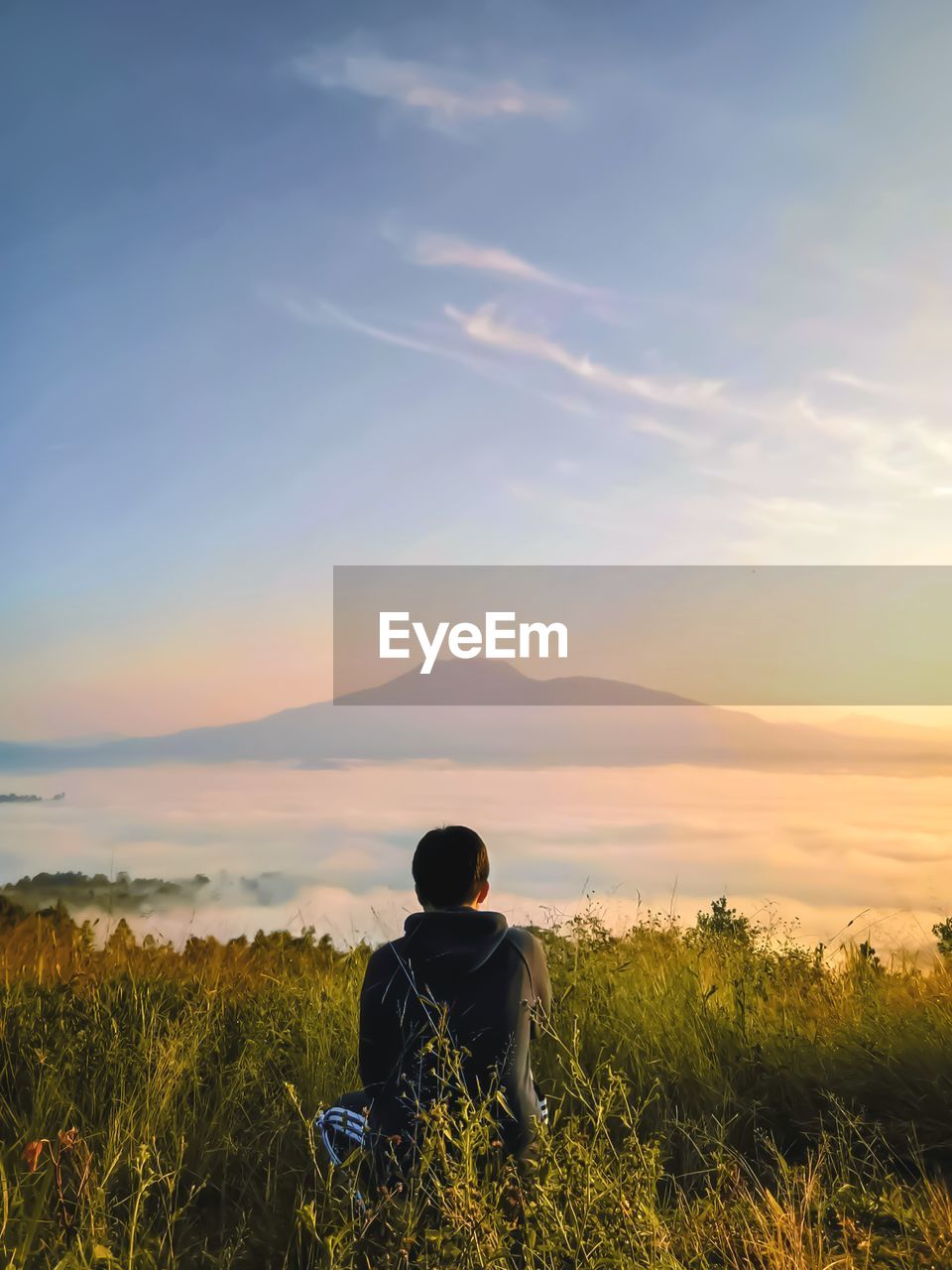 Rear view of man sitting on field against sky during sunset.west lampung, indonesia.