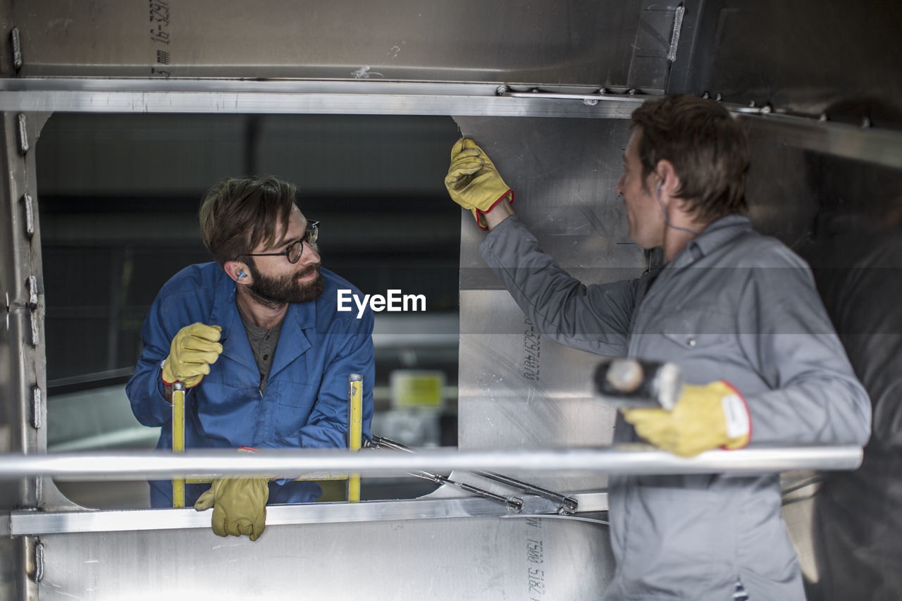 Two men discussing inside of steel container in factory