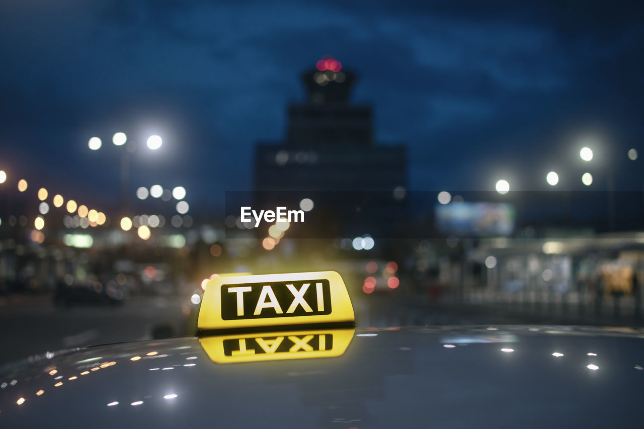 Taxi sign. reflection in roof of car against airport terminal building at night.