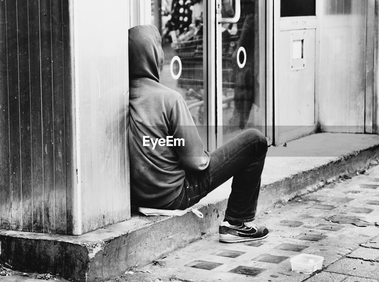 Man wearing hooded shirt sitting outside shop