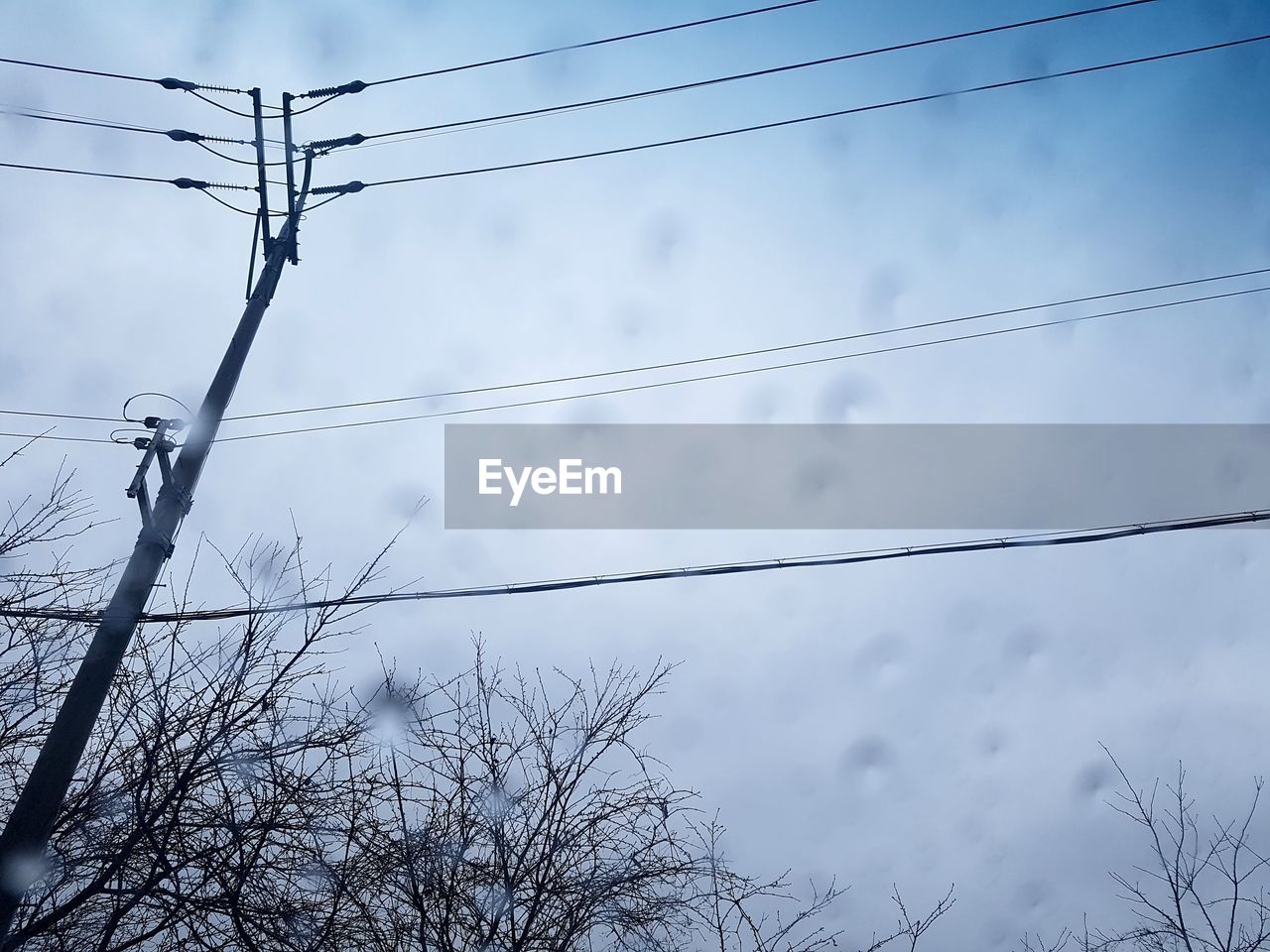 LOW ANGLE VIEW OF BIRD PERCHING ON CABLE AGAINST SKY