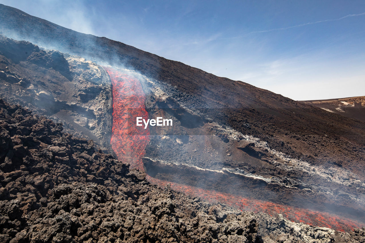 Incancecent lava flow  on etna volcano in sicily in valle del bove with smoke and lava flow canal
