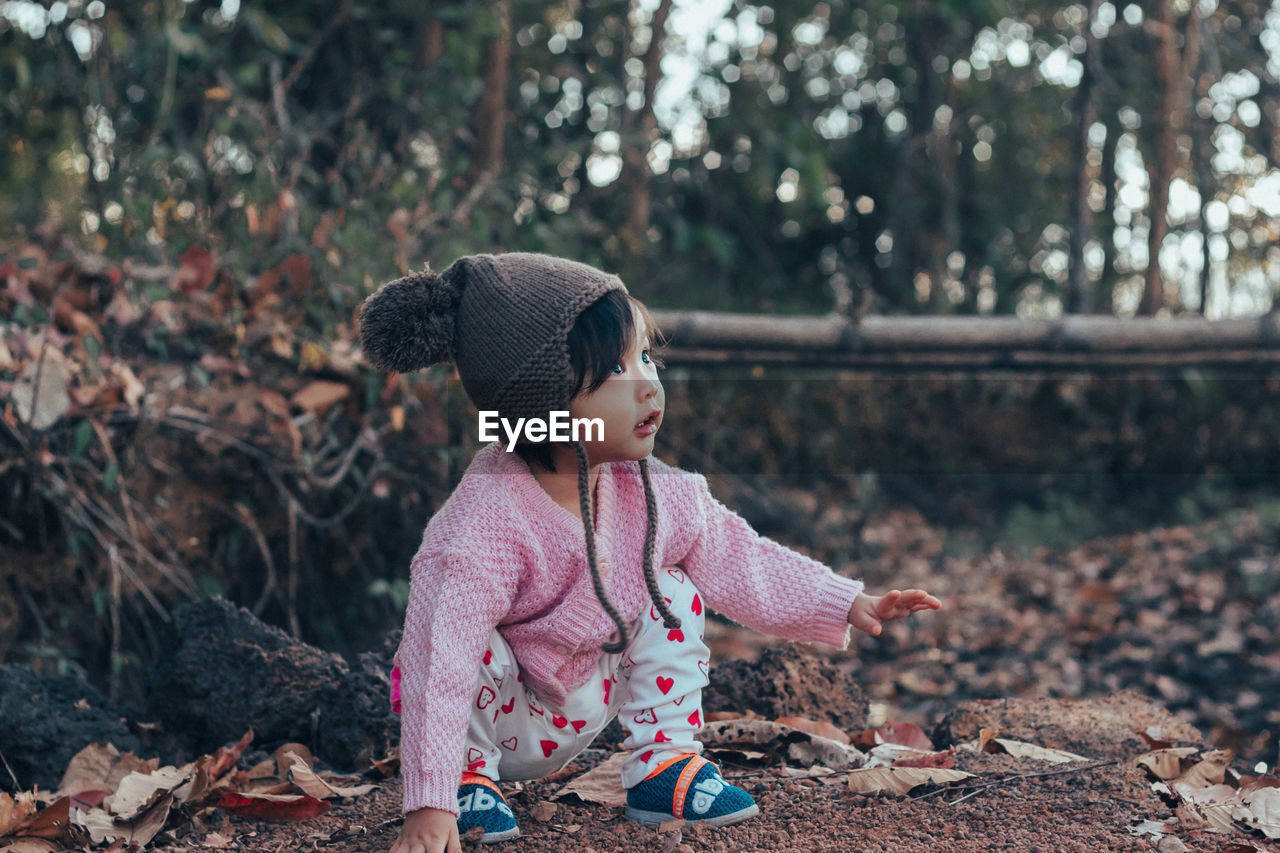 Cute baby girl looking away while crouching on land during winter