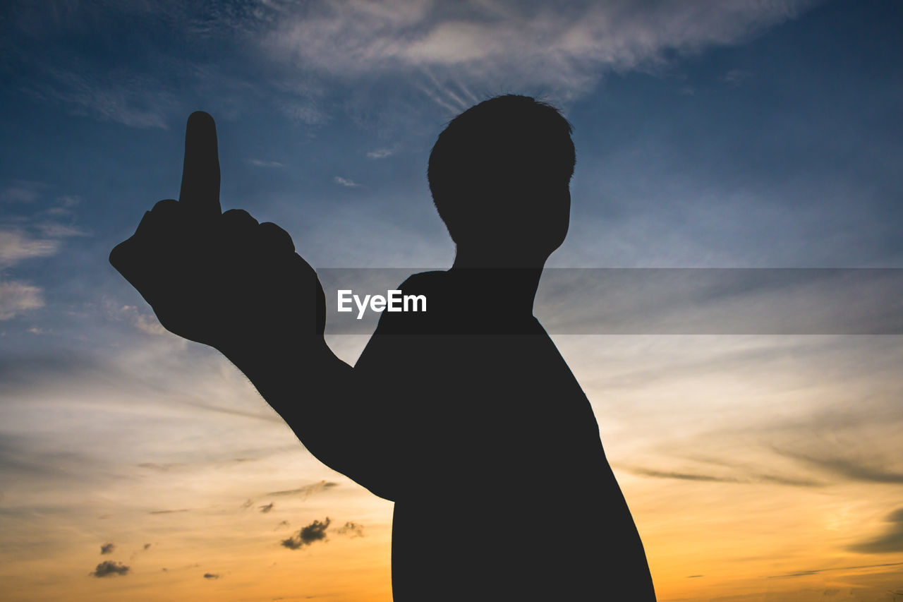 Silhouette man showing obscene gesture against sky during sunset