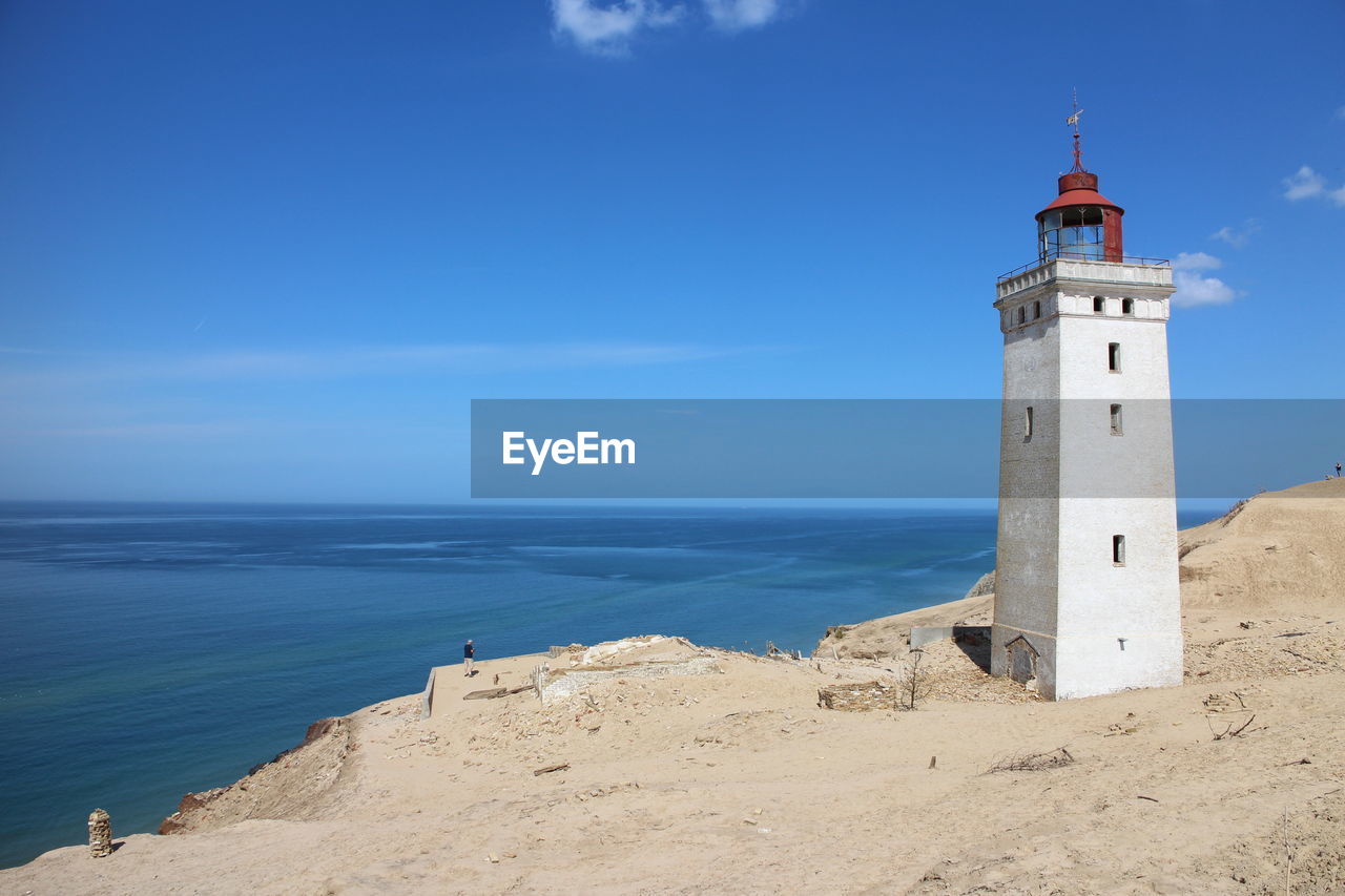 Lighthouse on beach against blue sky