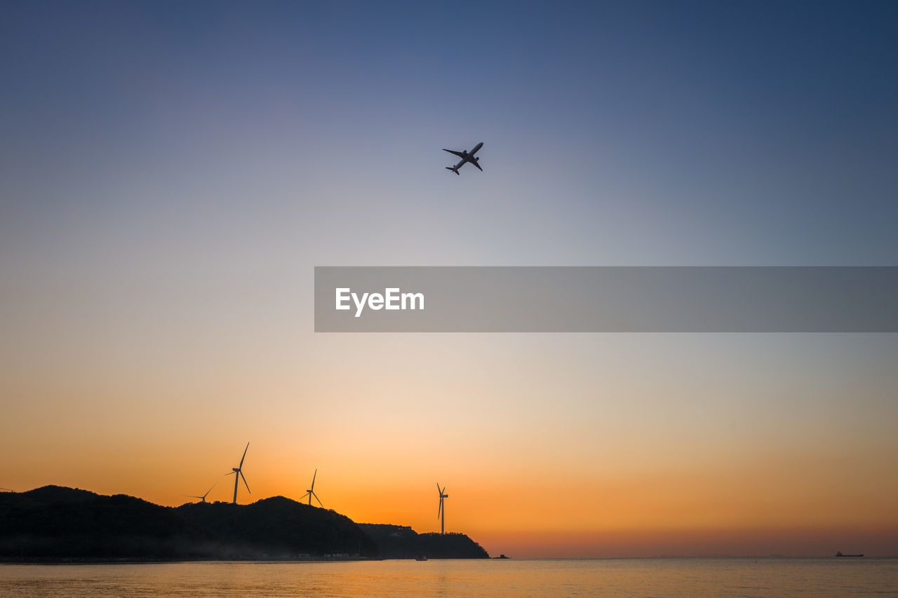 SILHOUETTE OF HELICOPTER IN SEA AGAINST SKY DURING SUNSET