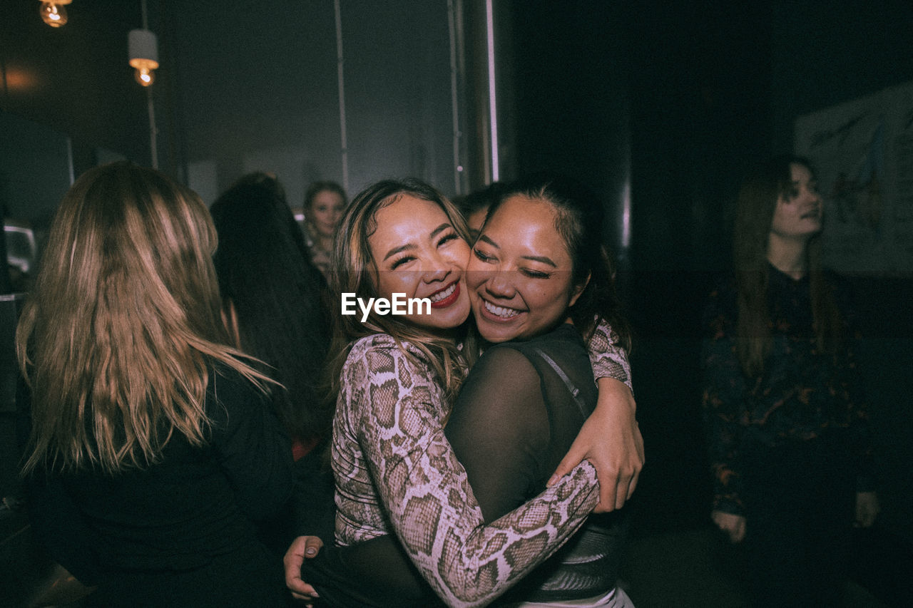 Portrait of cheerful young women embracing each other while enjoying at nightclub