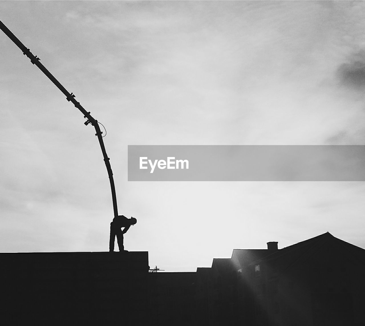 Silhouette man working with pipe on building terrace against sky