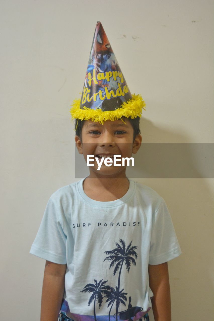 childhood, child, smiling, portrait, one person, happiness, yellow, front view, looking at camera, emotion, men, cheerful, standing, fun, waist up, clothing, innocence, toddler, indoors, celebration, teeth, smile, crown, casual clothing, studio shot, cute, female, hat, royalty, person, enjoyment, pride, t-shirt, costume, party hat, colored background, creativity