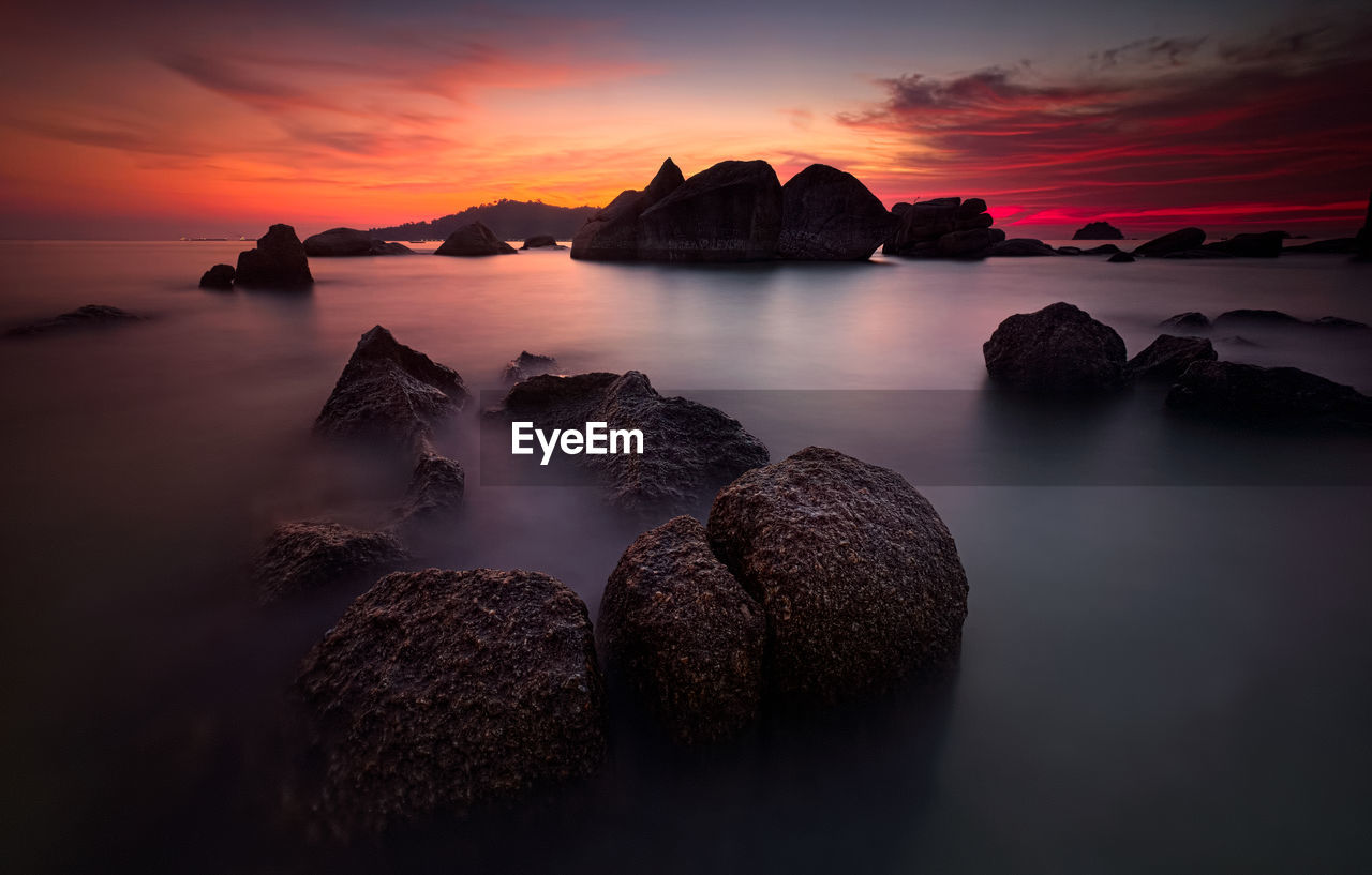 Rocks in sea against orange sky during sunset