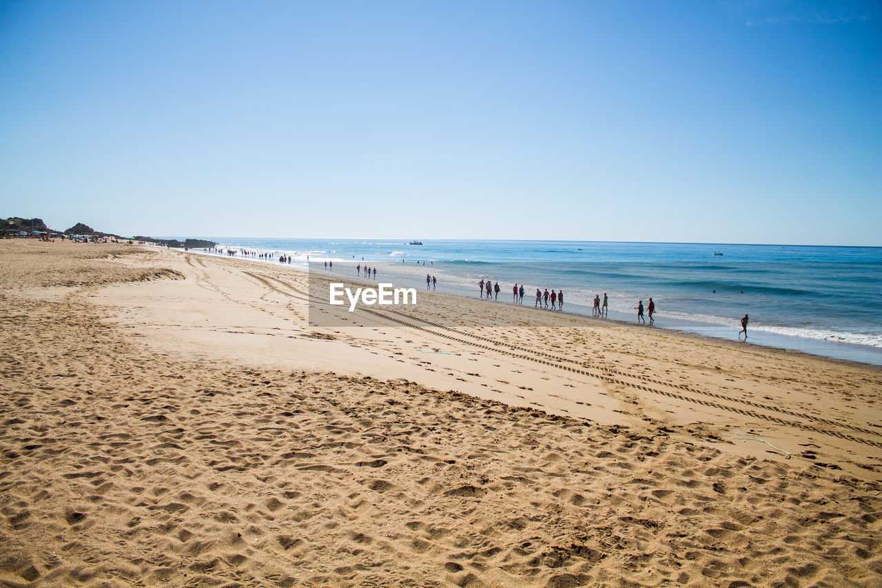 People on shore at beach against clear sky