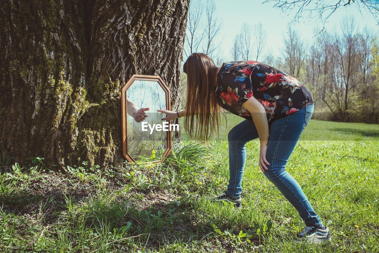 Woman touching picture frame against tree on field