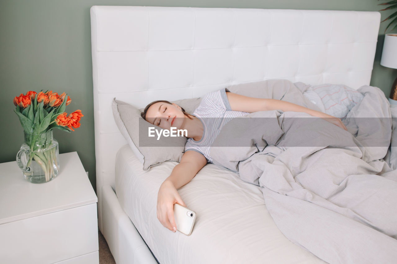 Woman lying in bed in morning with smartphone. digital online internet addiction.