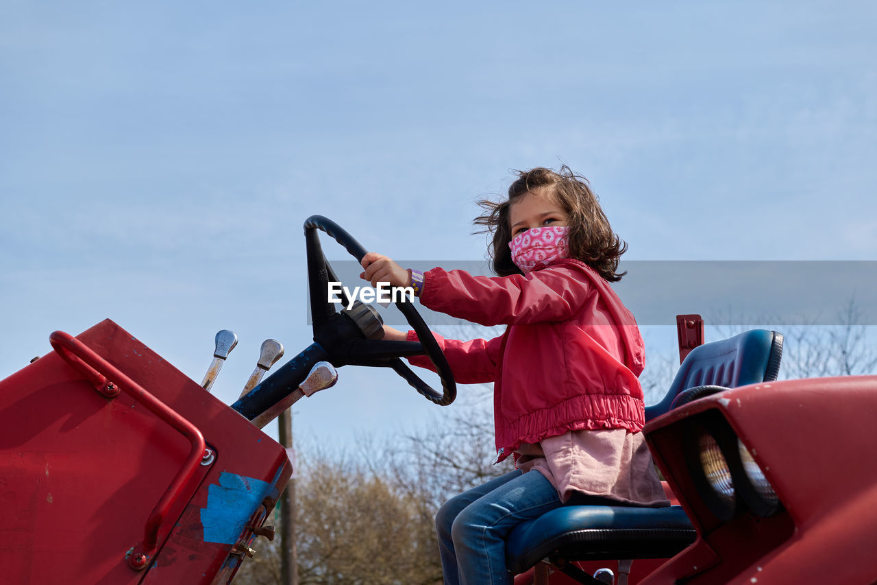 Girl in a mask pretending to drive a tractor at the county fair exhibit