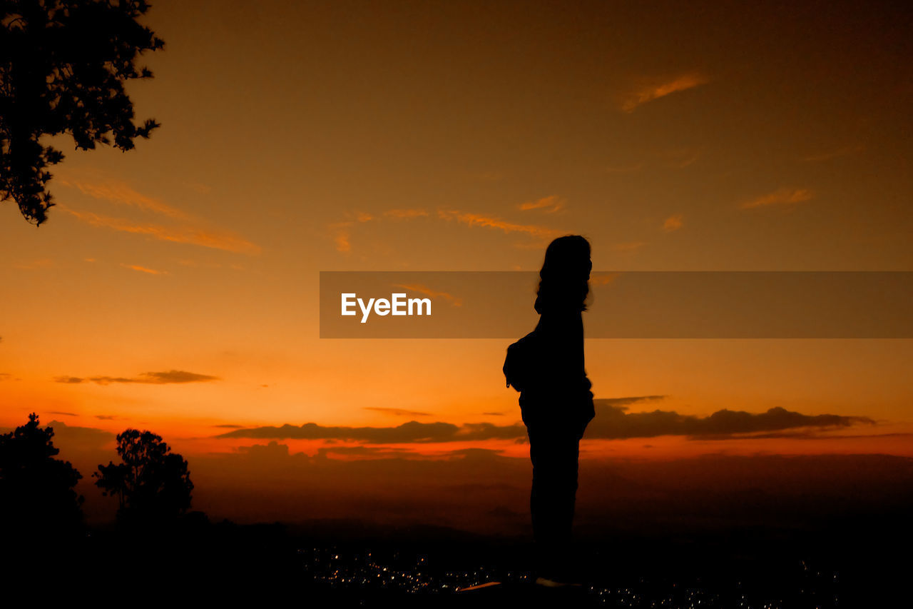 Silhouette woman standing on field against sky during sunset