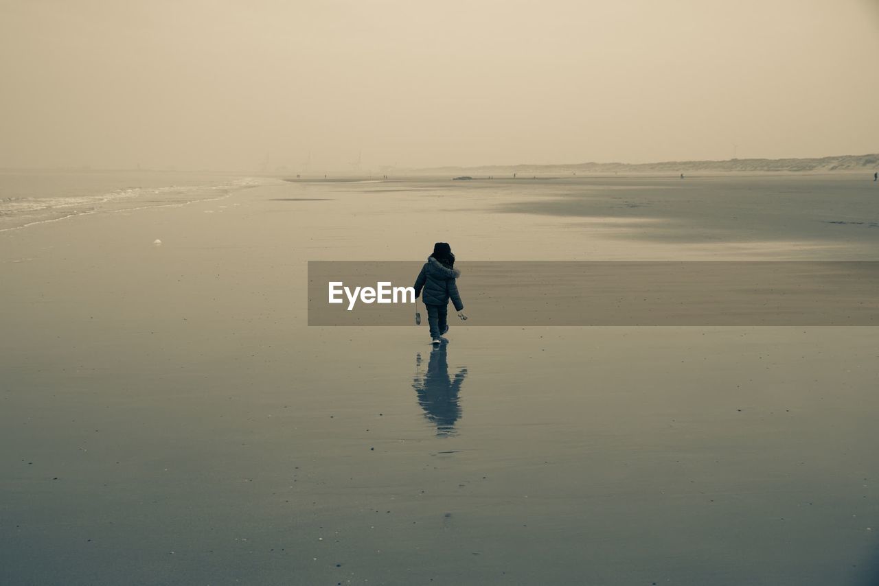 Rear view of boy walking at beach during sunset