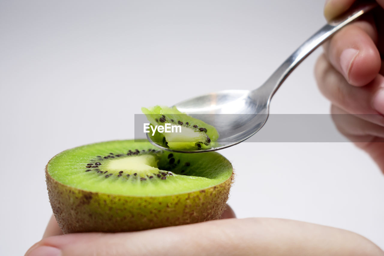 Cropped image of person eating kiwi against white background