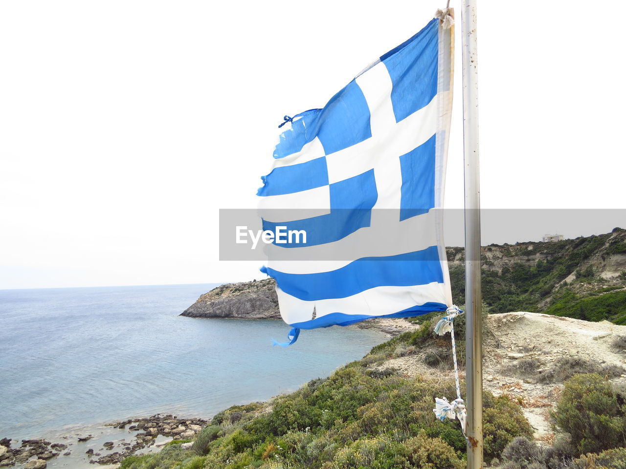 Greek flag waving by sea against clear sky