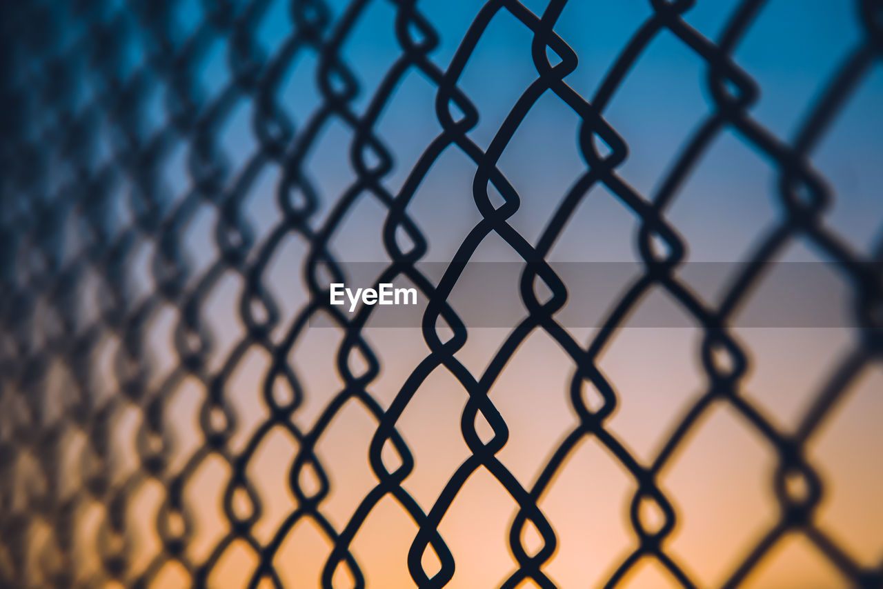 Close-up of chainlink fence against gradient sky