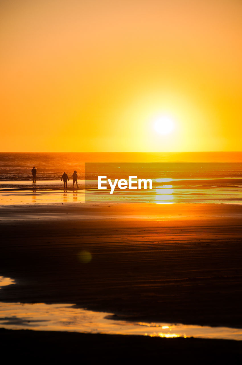 People at beach against sky during sunset