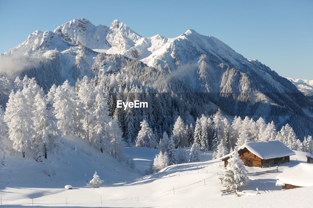 Picturesque winter scene with traditional alpine chalet and snowy mountains