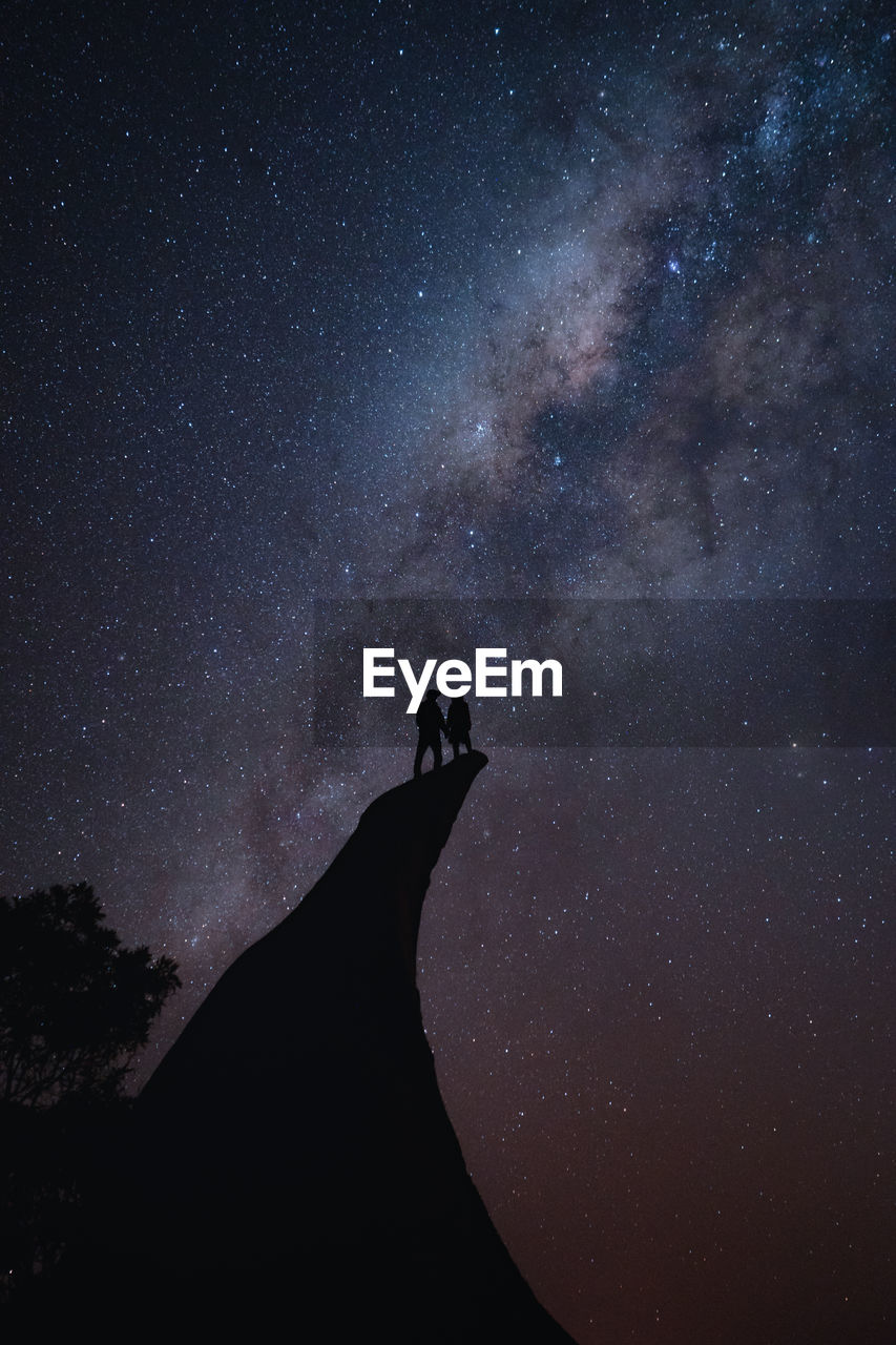 Couple standing on the edge of a cliff during the night sky