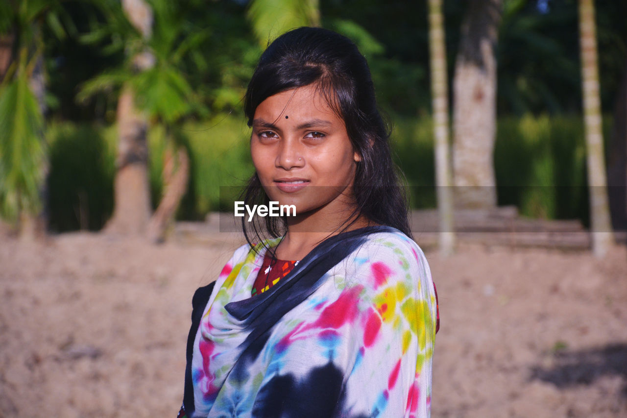 Portrait of young woman standing against trees