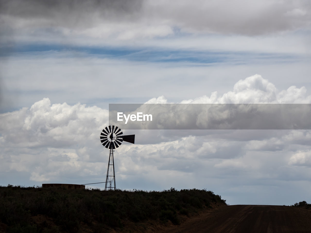 Silhouette windmill on land against sky