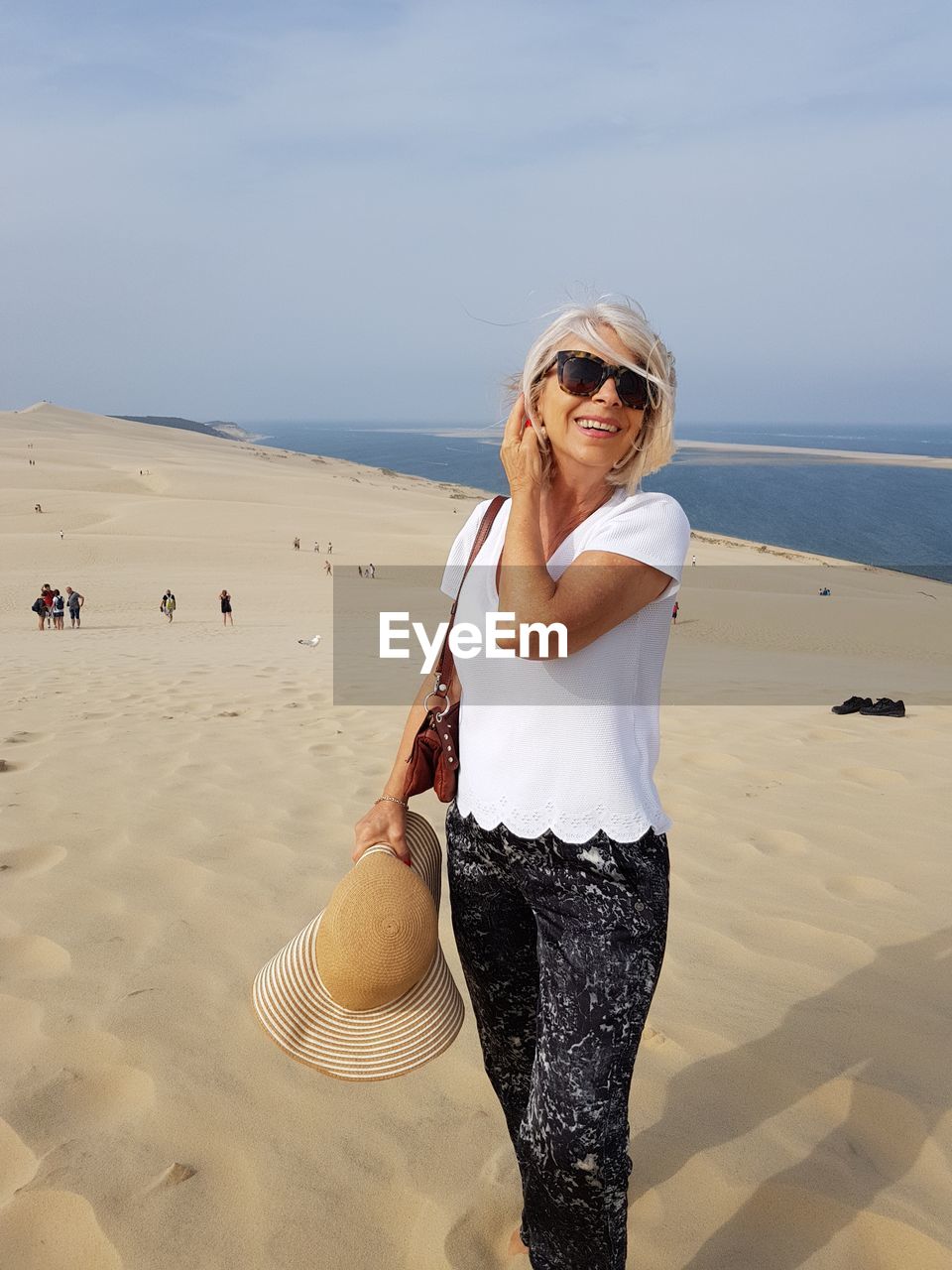 Portrait of woman wearing sunglasses while standing at beach against sky