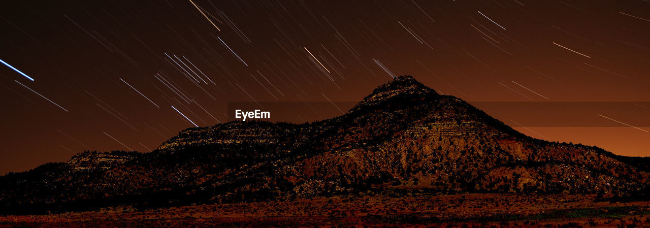Panoramic view of star trails over mountains at night