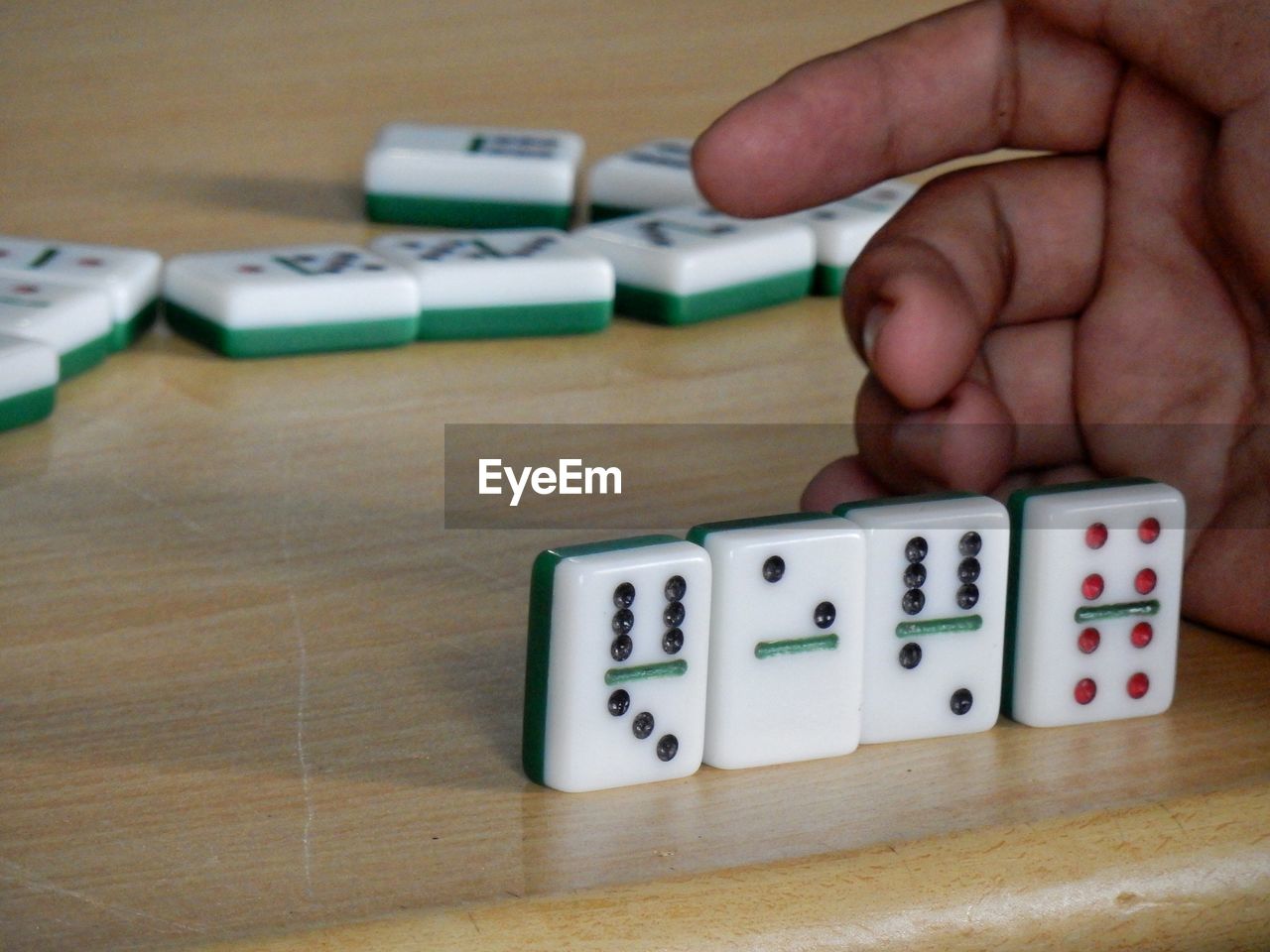 Close-up of human hand playing dominoes on wooden table
