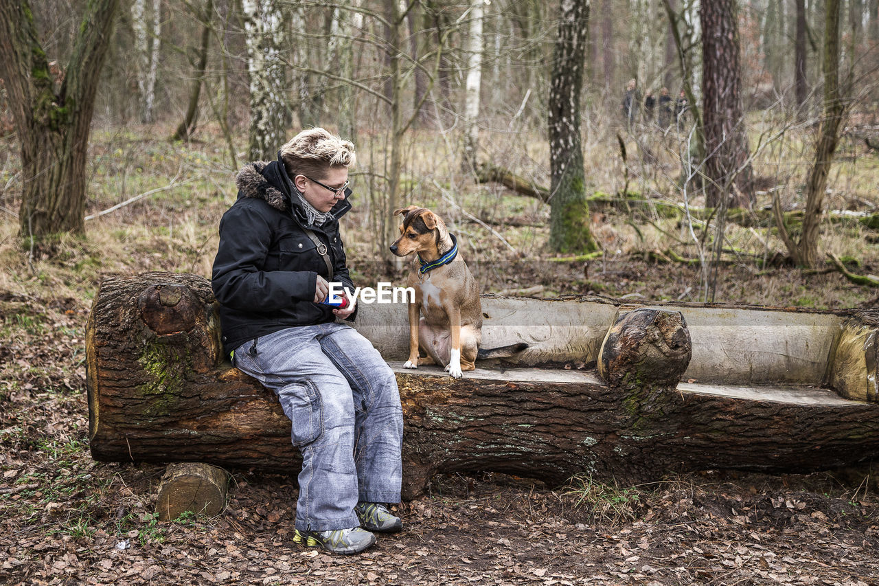 WOMAN WITH DOG SITTING ON TREE IN FOREST