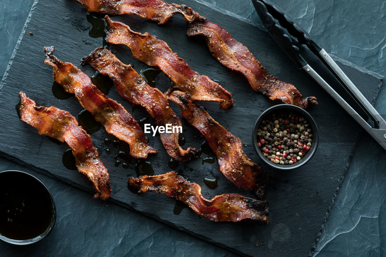 Wavy strips of crispy maple cracked peppercorn bacon on a black slate board.