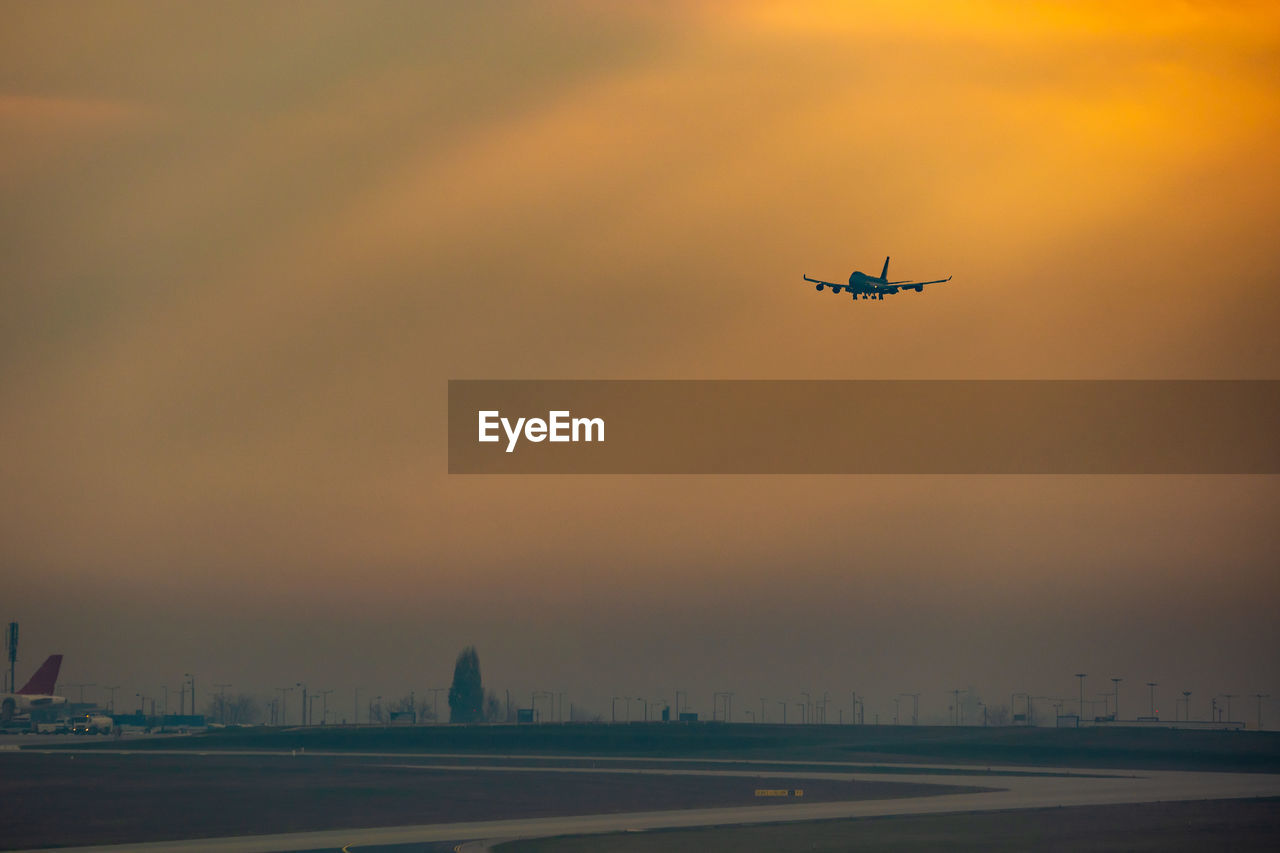 LOW ANGLE VIEW OF AIRPLANE AGAINST SKY DURING SUNSET