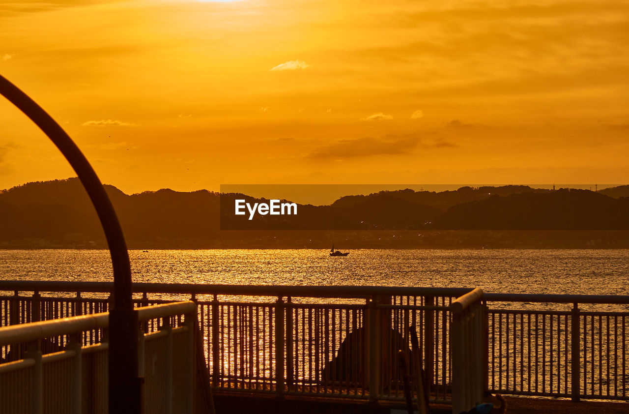 Silhouette railing by sea against orange sky