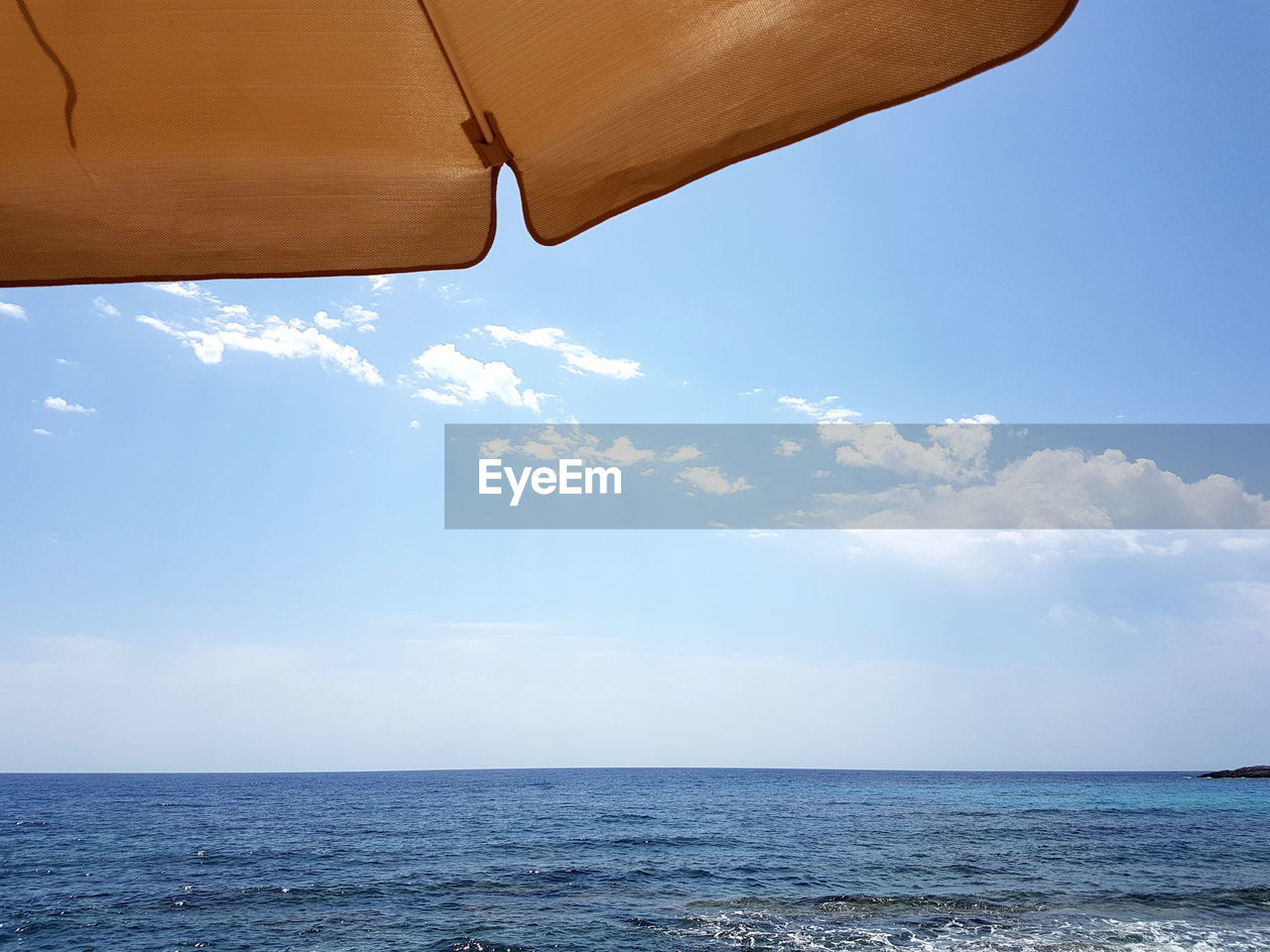 Cropped image of parasol by sea against sky