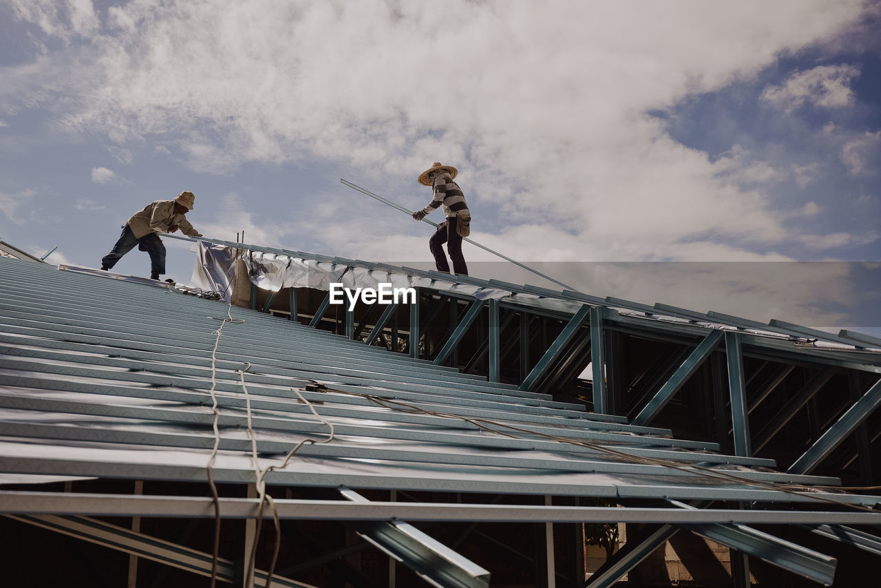 Low angle view of men working on rooftop against sky