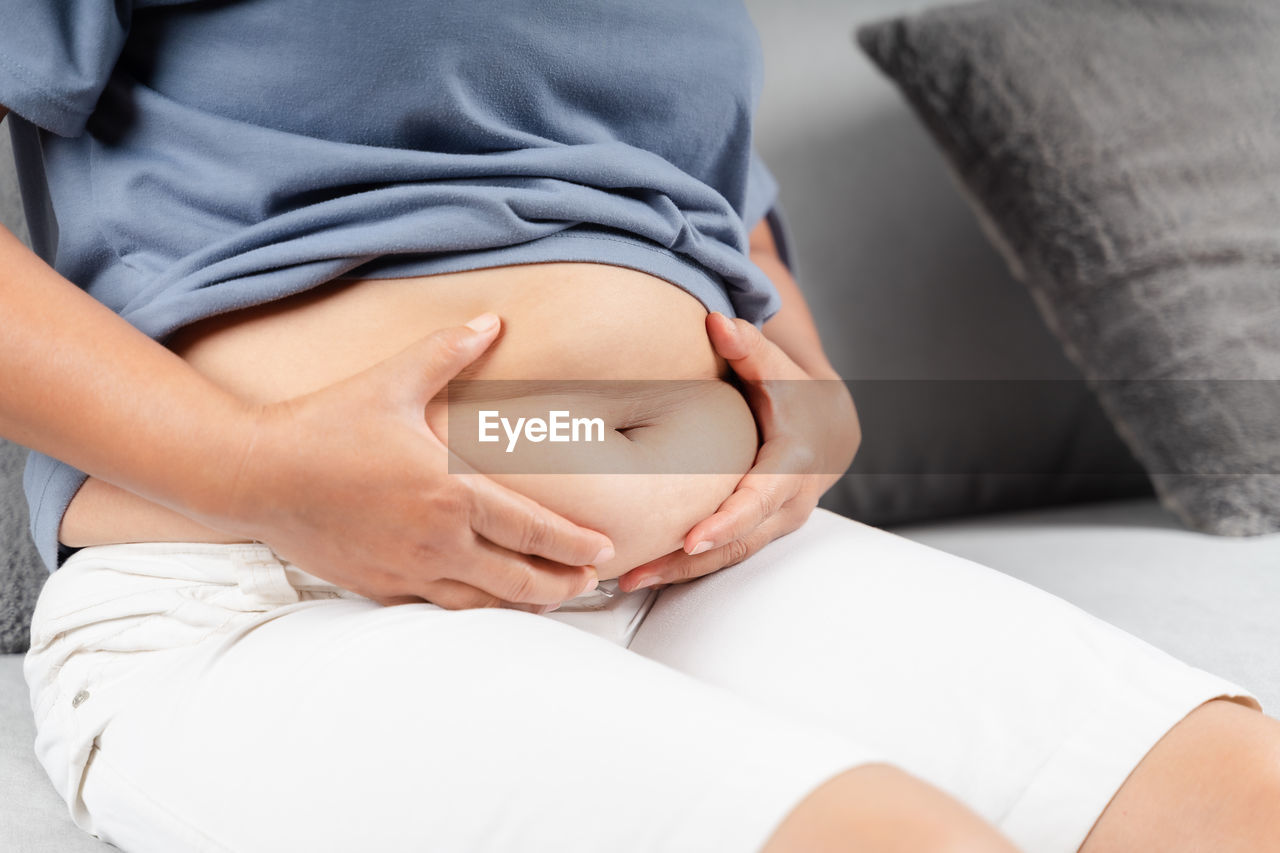 MIDSECTION OF WOMAN LYING DOWN ON BED